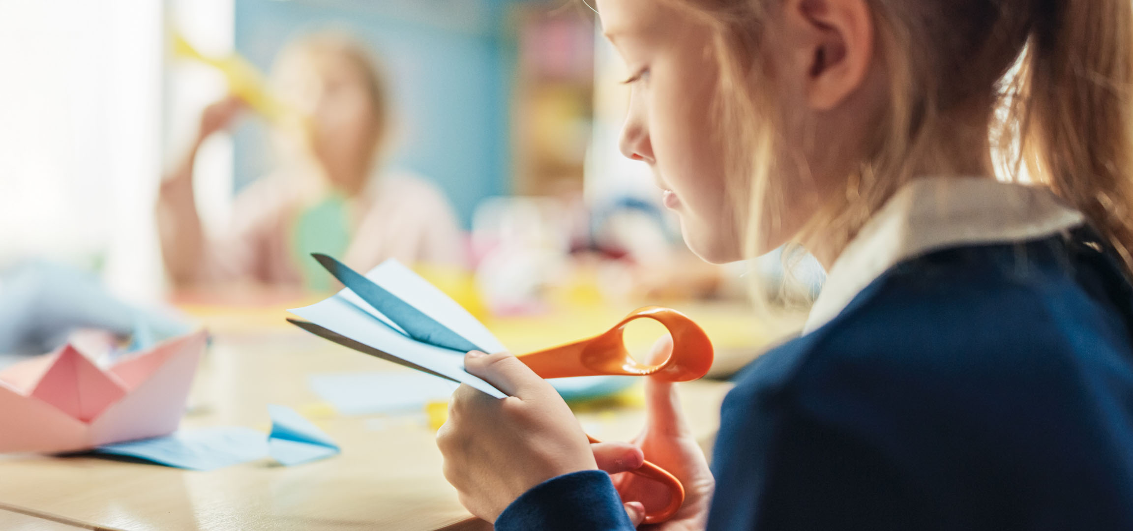Una bambina taglia la carta per creare barche origami colorate.