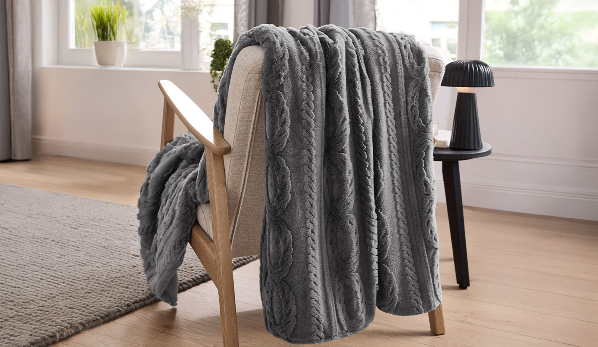 Una coperta grigia a trecce drappeggiata su una poltrona in legno chiaro in soggiorno.