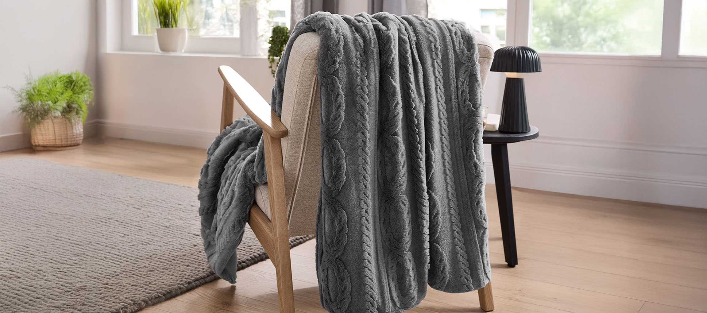 Plaid grigio a trecce drappeggiato su una poltrona in legno chiaro in una stanza luminosa.