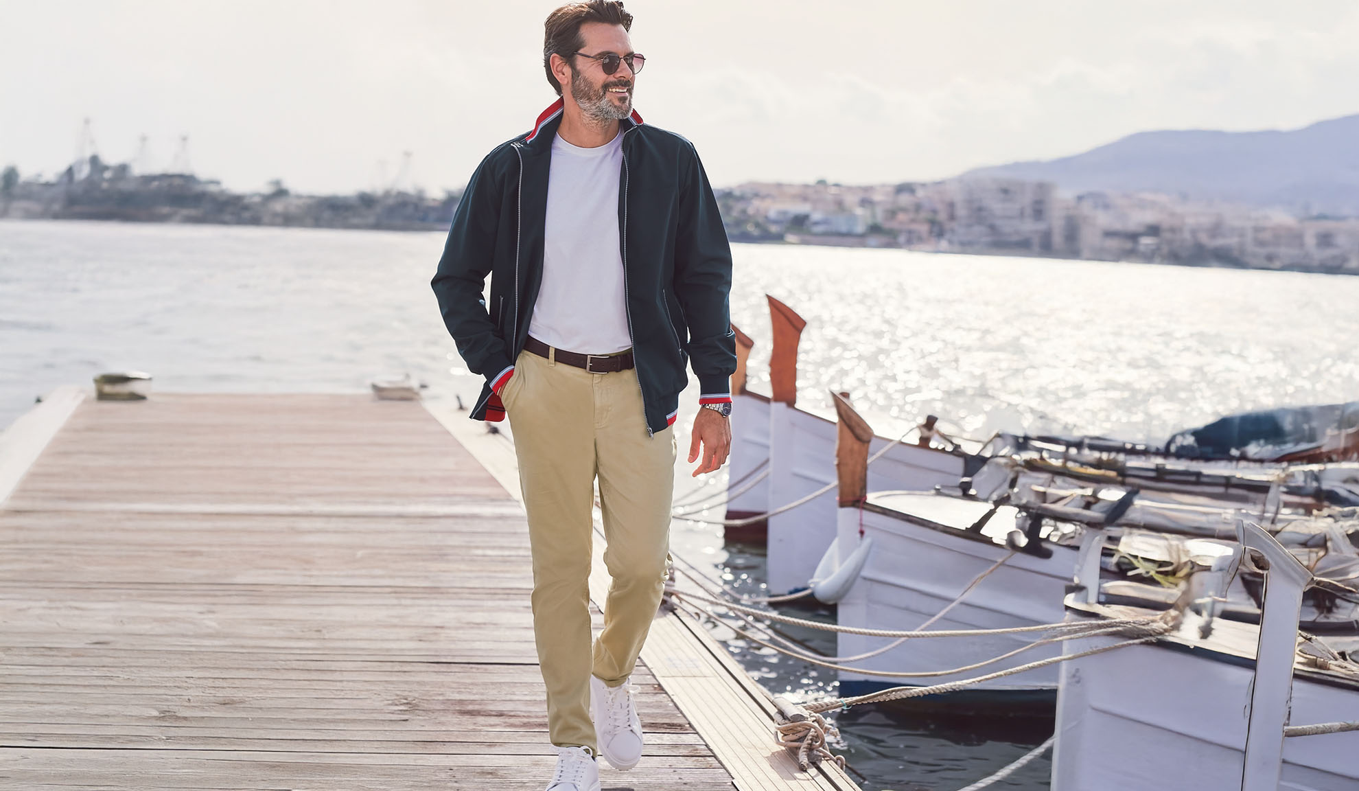 Uomo in giacca blu navy, maglietta bianca e pantaloni kaki su un molo.
