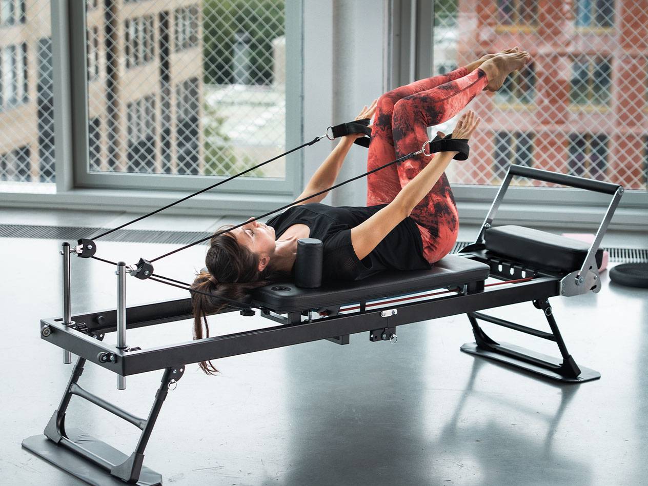 Donna che fa Pilates su un reformer con pantaloni da yoga rossi.