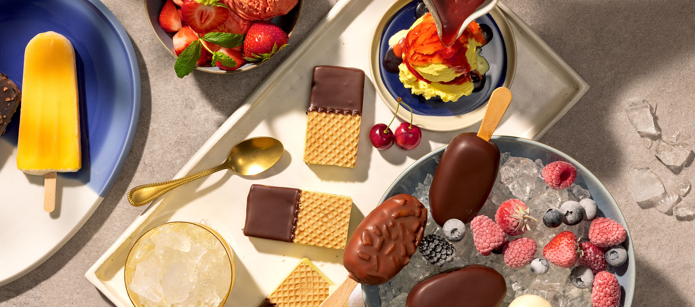 Assortimento di gelati su stecco, palline di gelato e wafer ricoperti di cioccolato con frutti di bosco.