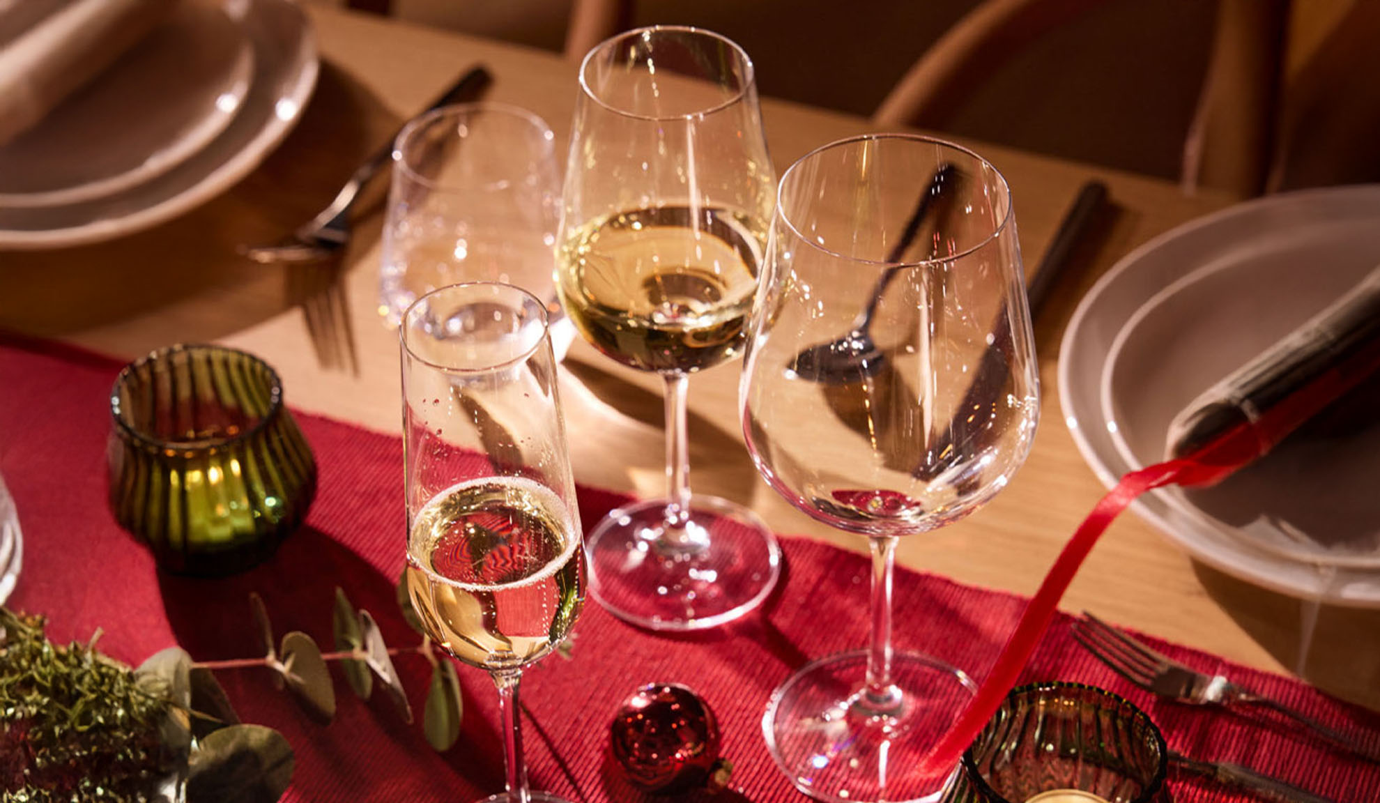 Tavola festiva apparecchiata con calici da vino, flûte da champagne e decorazioni natalizie.