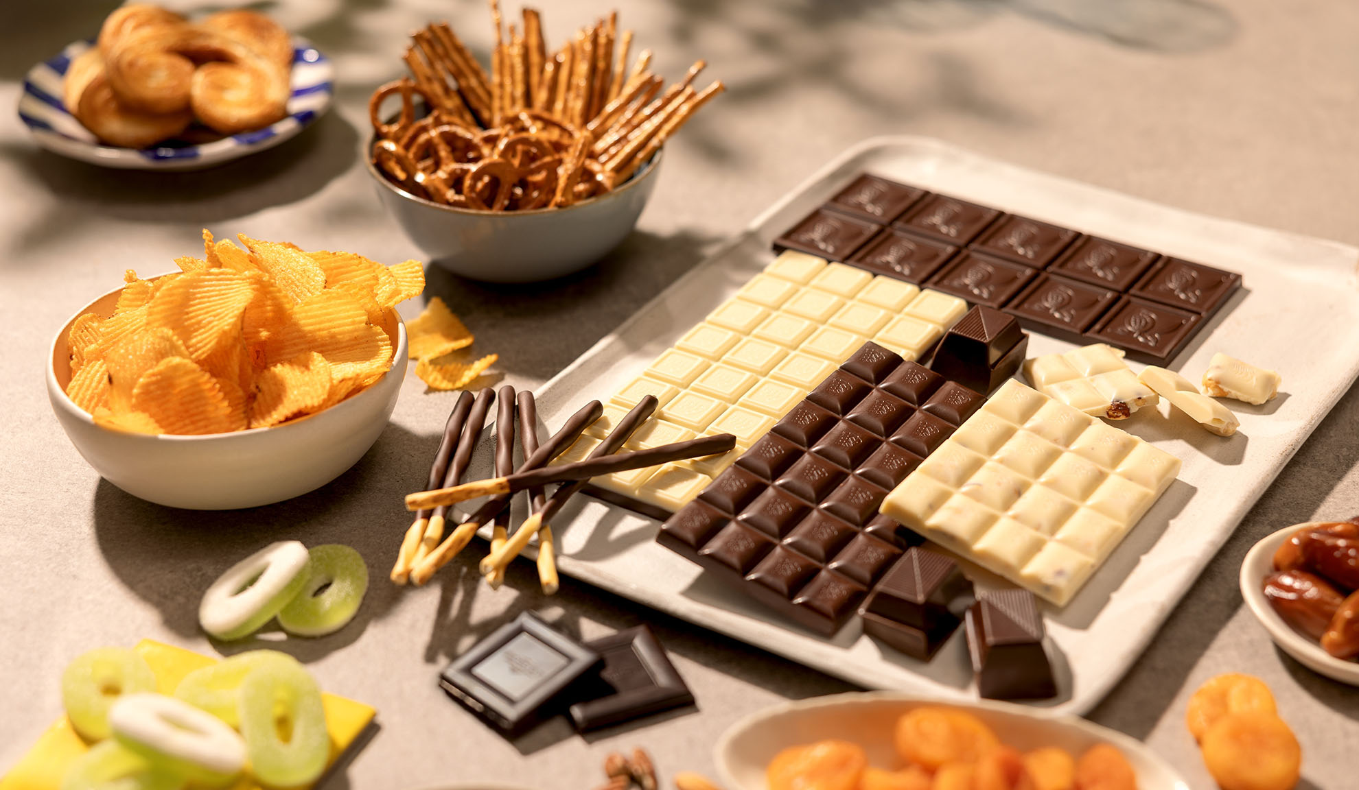 Un assortimento di snack tra cui tavolette di cioccolato, patatine, pretzel e dolci.