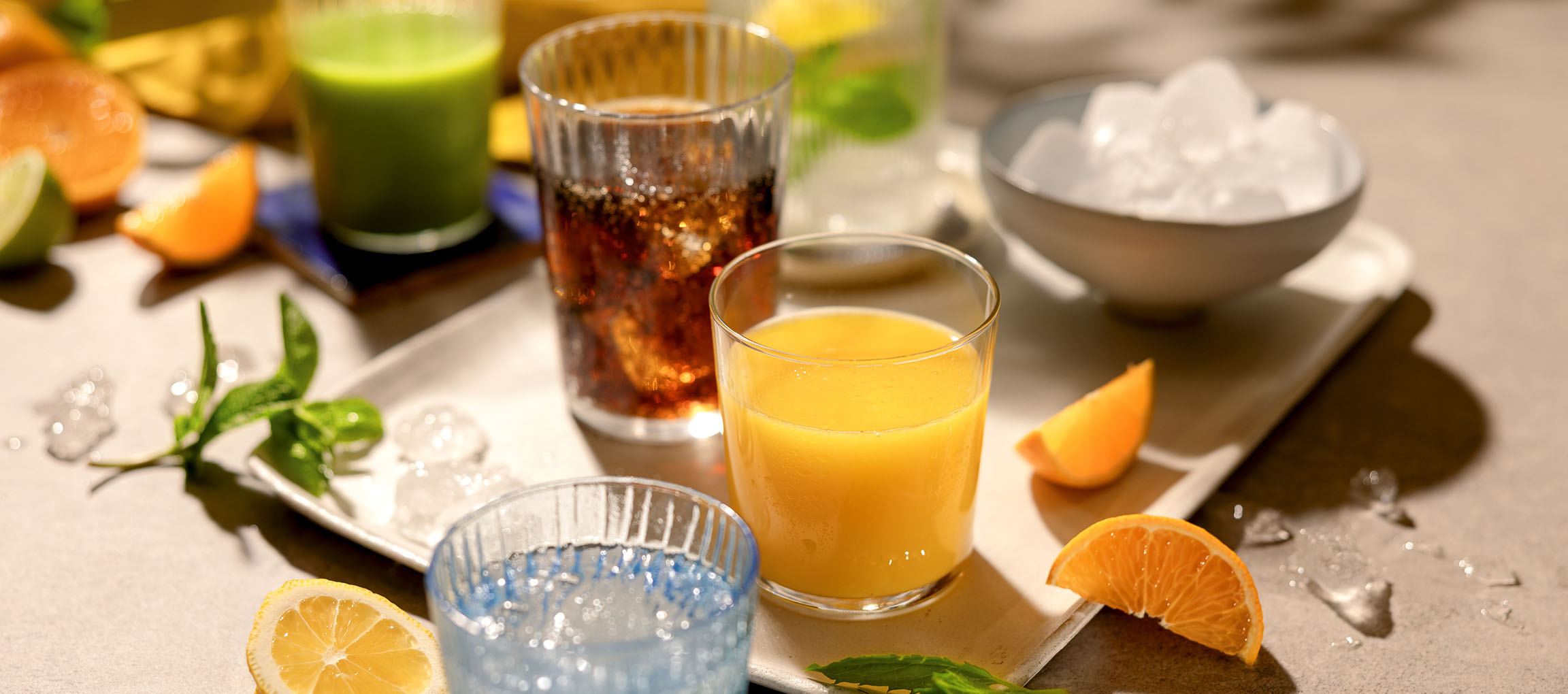 Varie bevande rinfrescanti e frutta su un vassoio, inclusi succo d'arancia e bevande gassate.