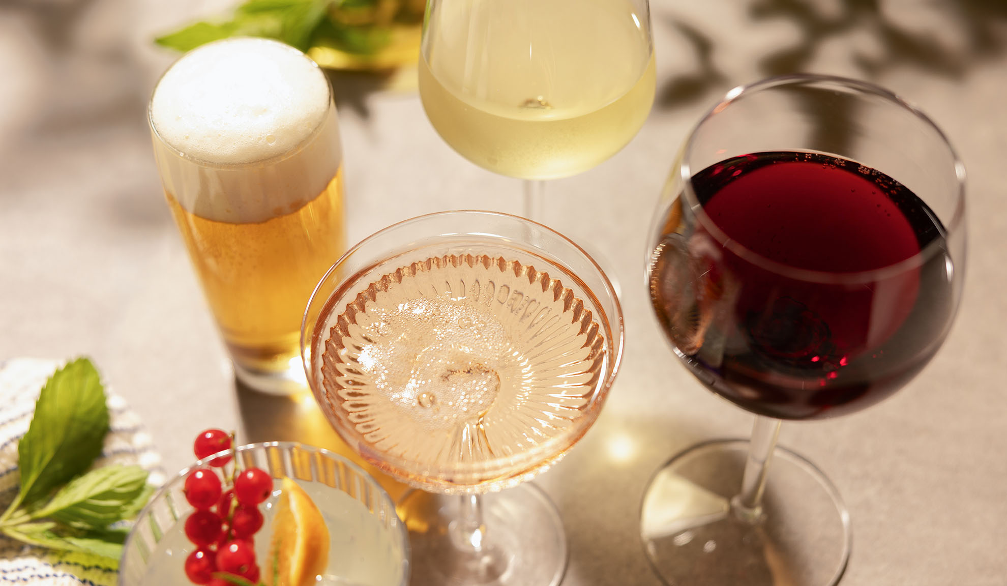 Bicchieri di birra, vino bianco, rosé e rosso, con un cocktail e bacche.