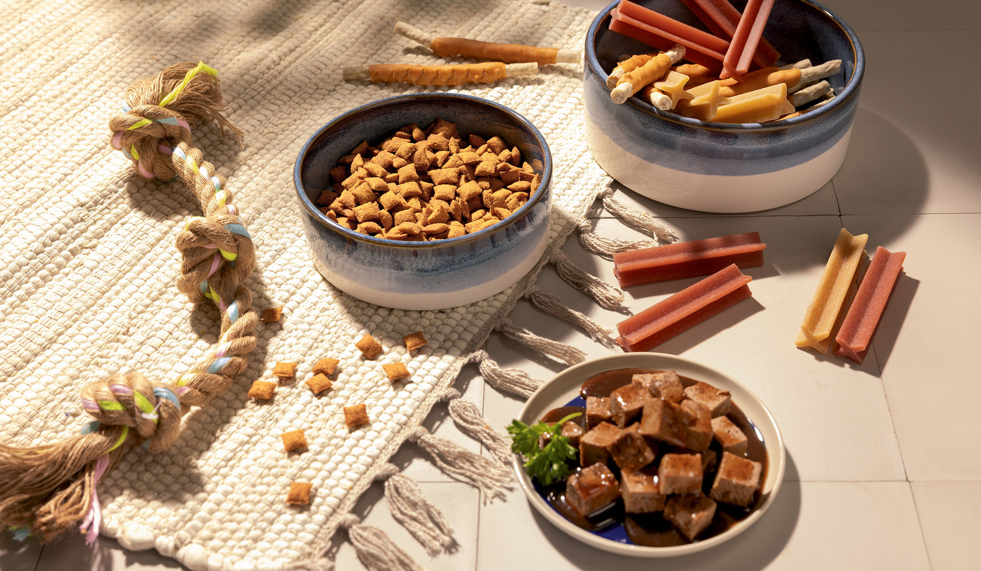 Assortimento di cibo e snack per animali domestici, inclusi crocchette, cibo umido e bastoncini da masticare.