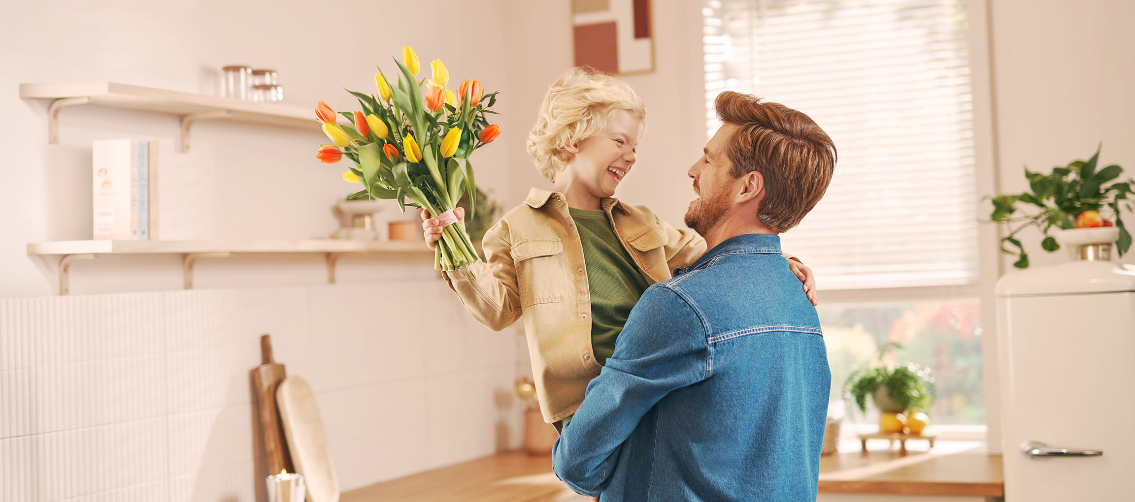 Un bambino con un mazzo di tulipani, che ride con un uomo in cucina.