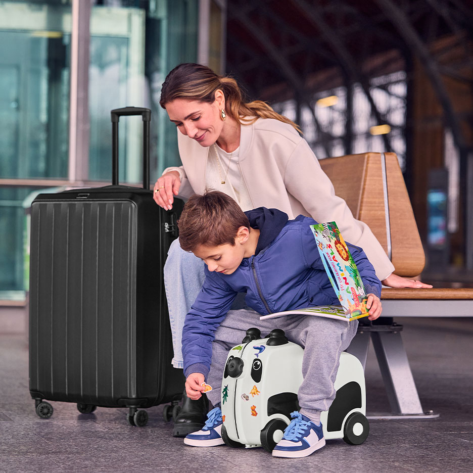 Donna e bambino con grande valigia nera e valigia cavalcabile a forma di panda in aeroporto.