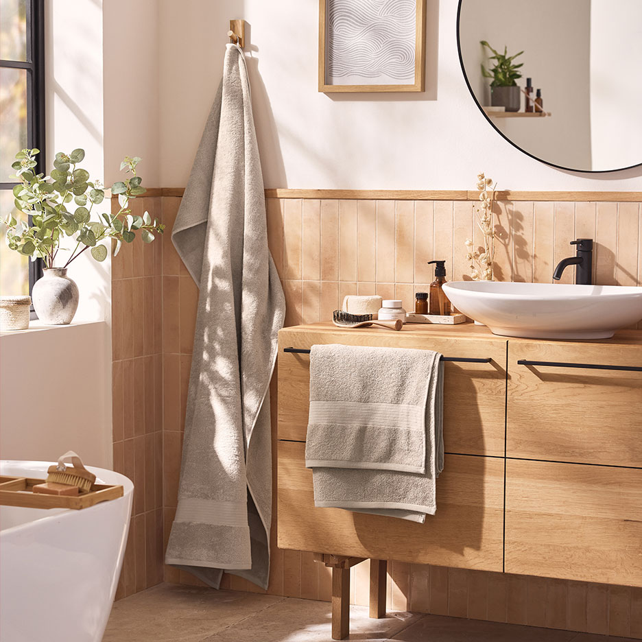 Bagno moderno con asciugamani beige, lavabo bianco e mobili in legno.