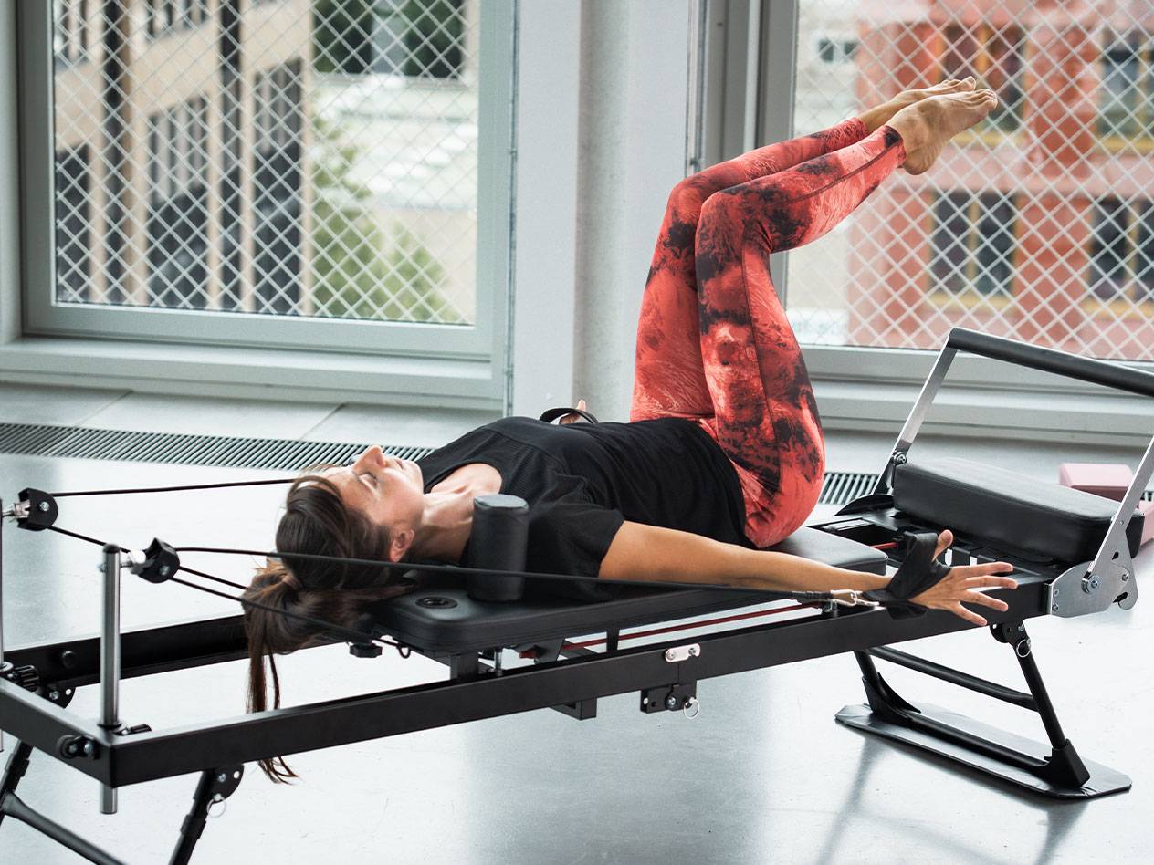 Donna che fa Pilates su un reformer, con leggings rossi e neri