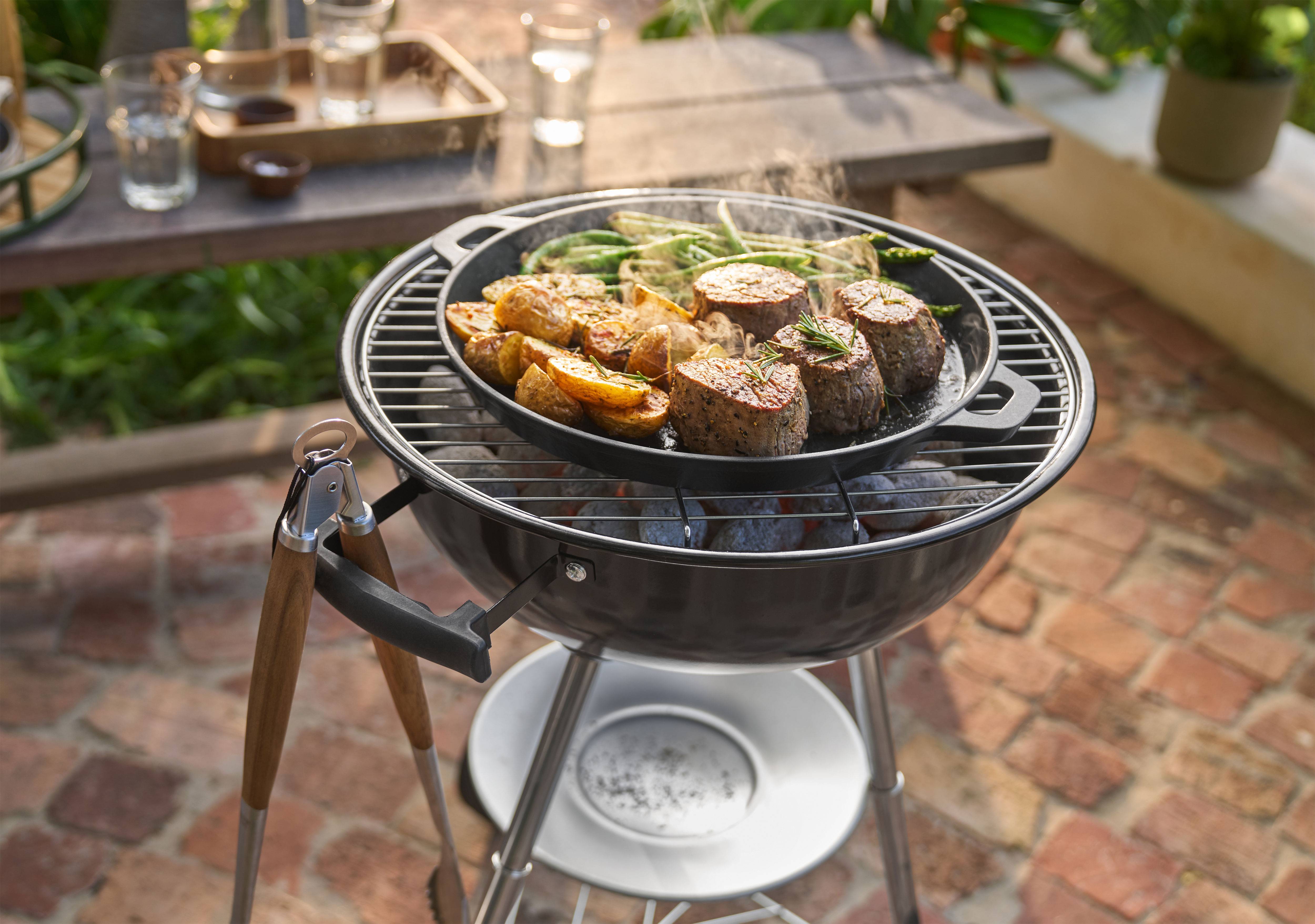 Barbecue con carne, patate e fagiolini che cuociono in padella all'aperto.