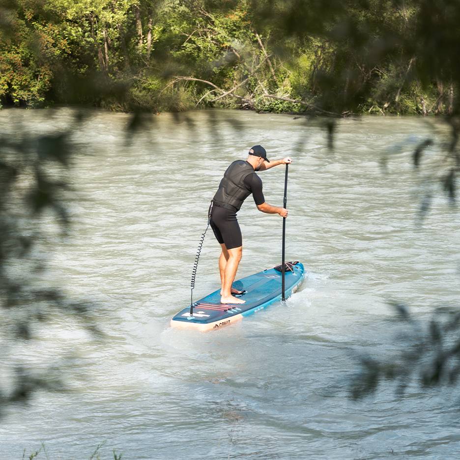 Uomo in muta e giubbotto di salvataggio che pagaia su una tavola da SUP blu in un fiume.