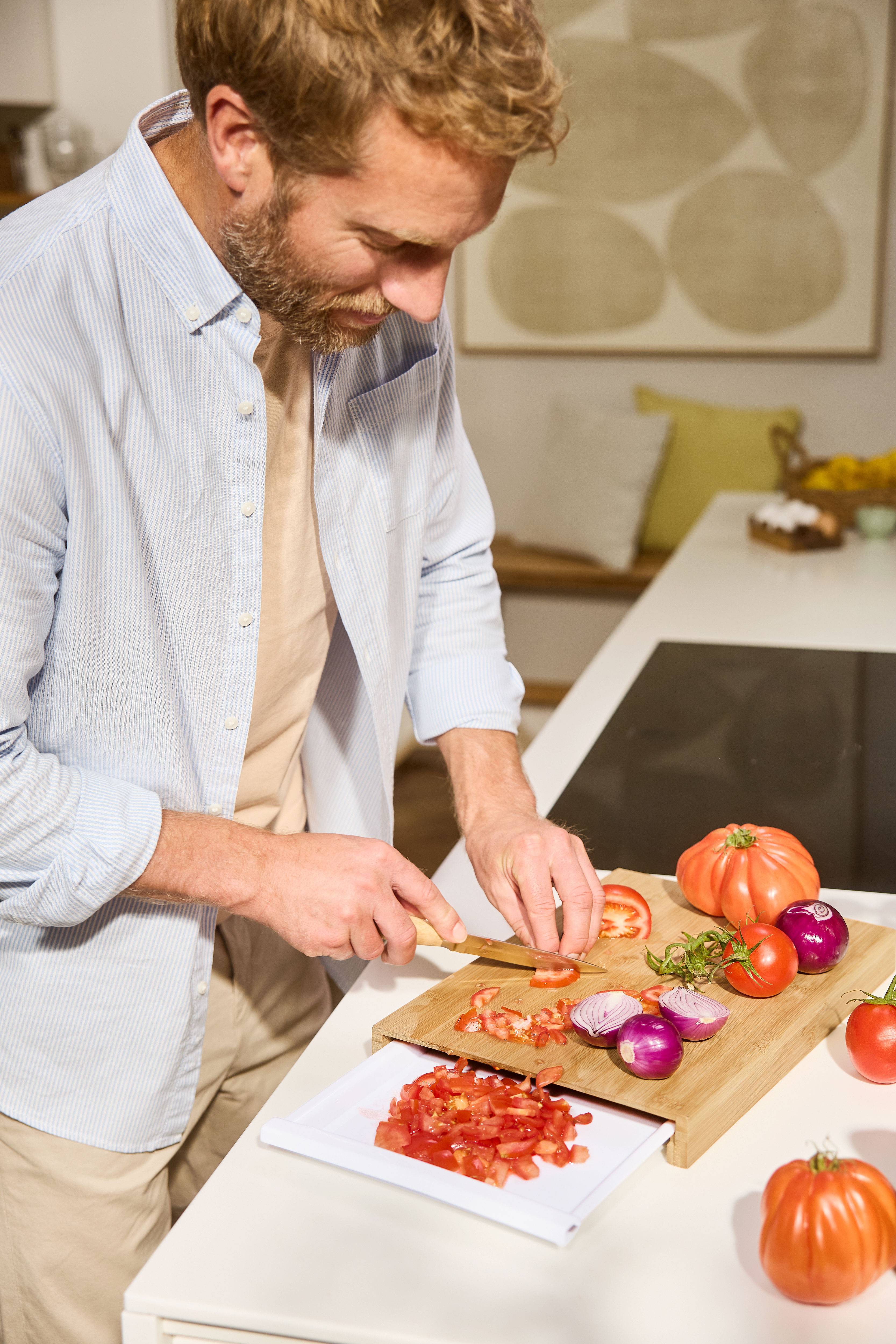 Uomo che taglia pomodori e cipolle su un tagliere di legno in cucina.