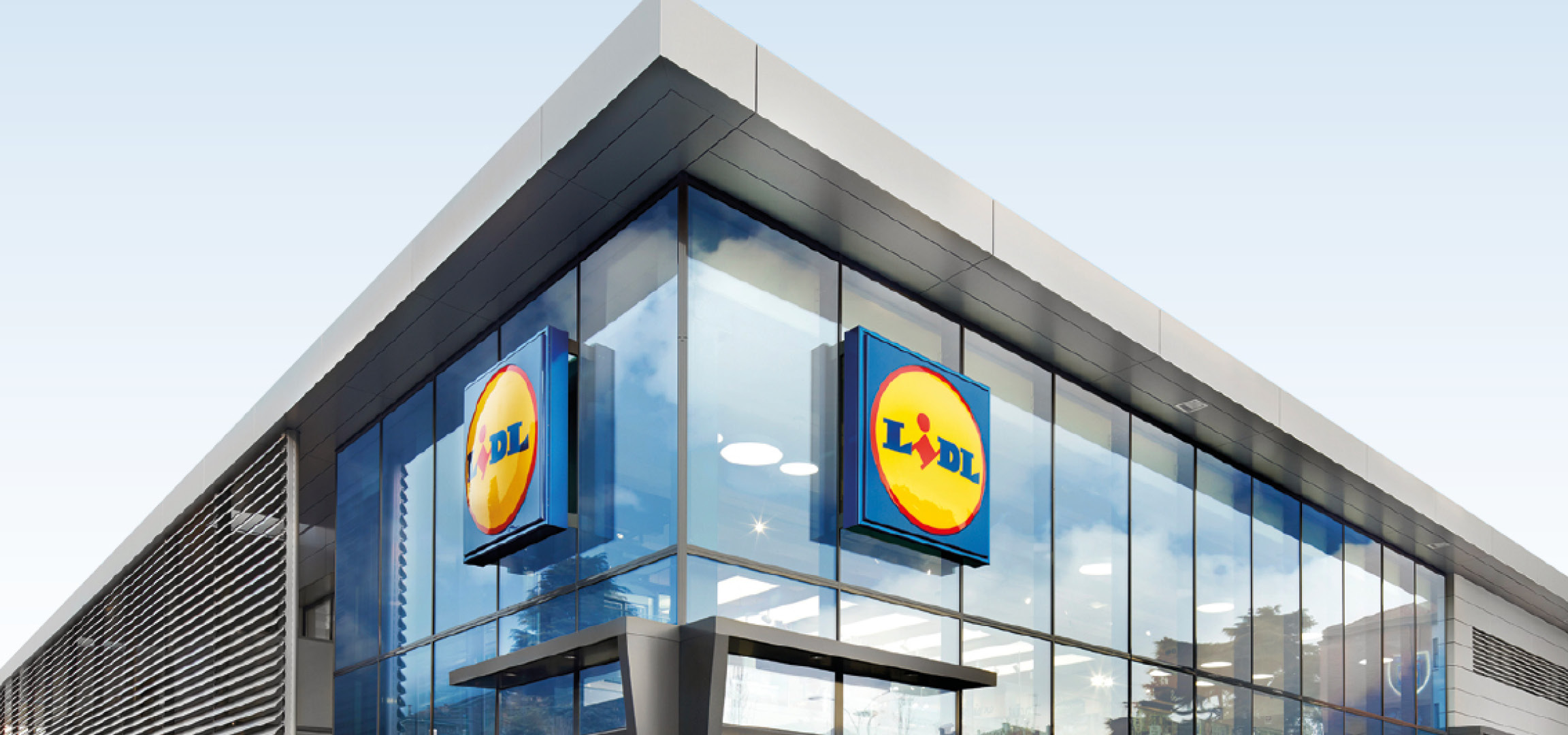 Insegne Lidl su un moderno edificio in vetro con cielo azzurro riflesso.