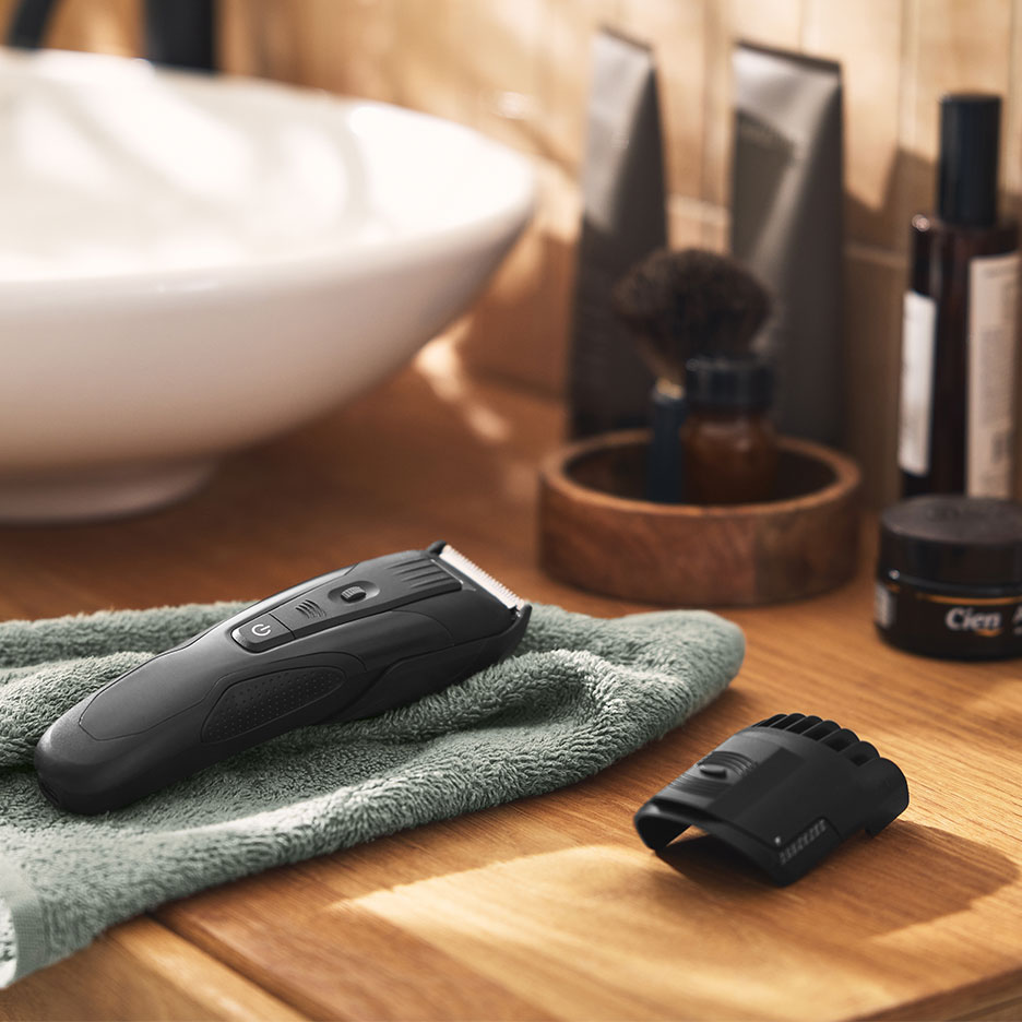Rasoio elettrico nero su un asciugamano verde in bagno con lavandino e prodotti per la cura.