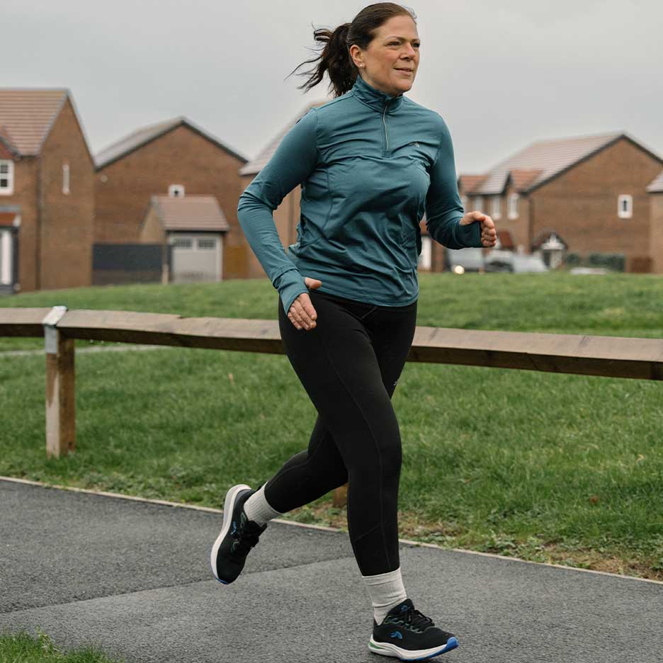 Donna in abbigliamento sportivo che corre su un sentiero all'aperto.