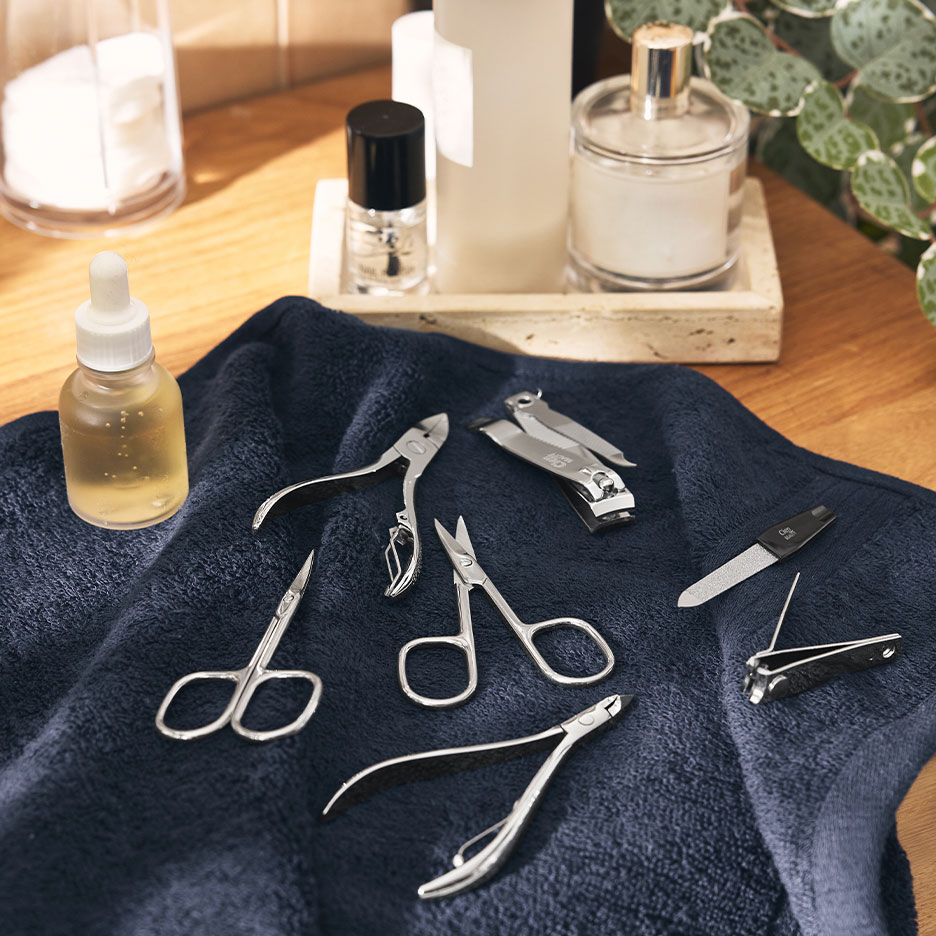 Set manicure con tagliaunghie, forbici e lime su un asciugamano blu scuro.