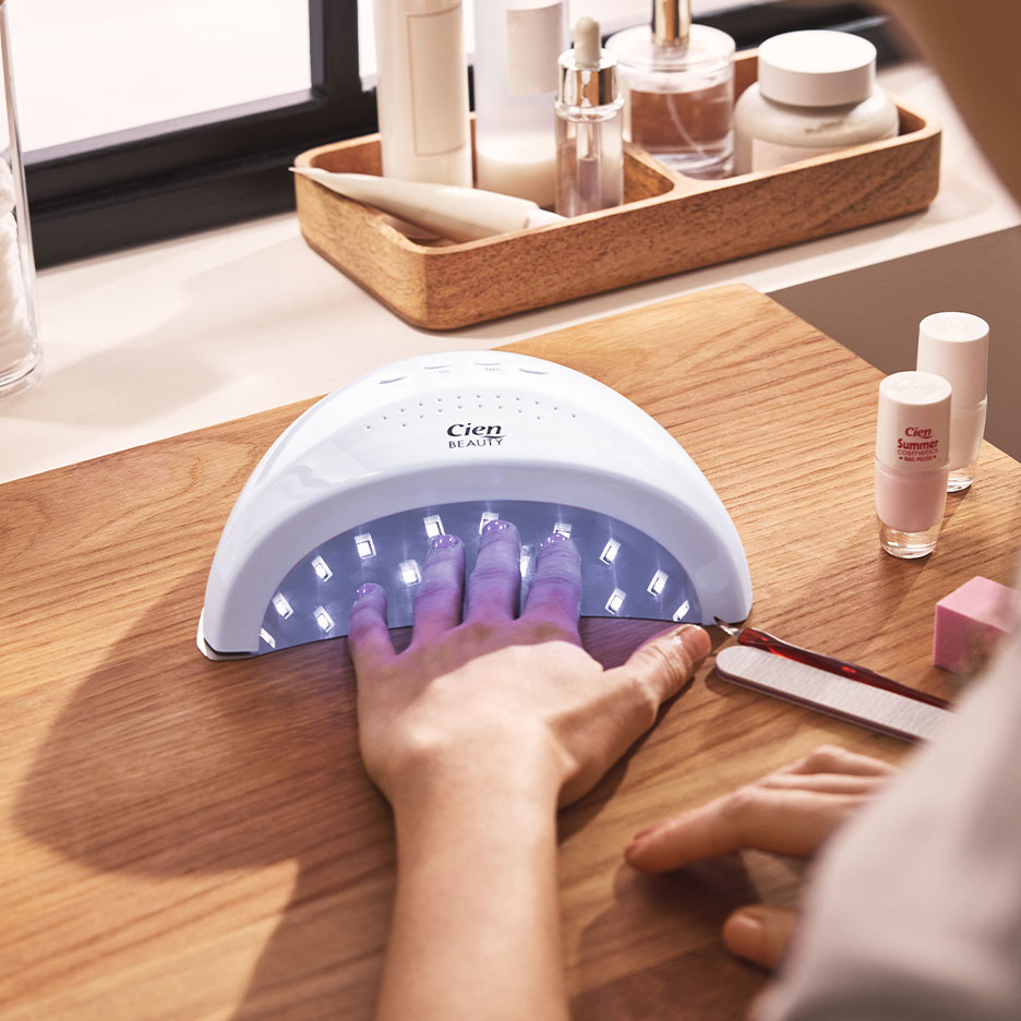 Donna che asciuga le unghie in una lampada UV, con smalti e accessori per manicure.
