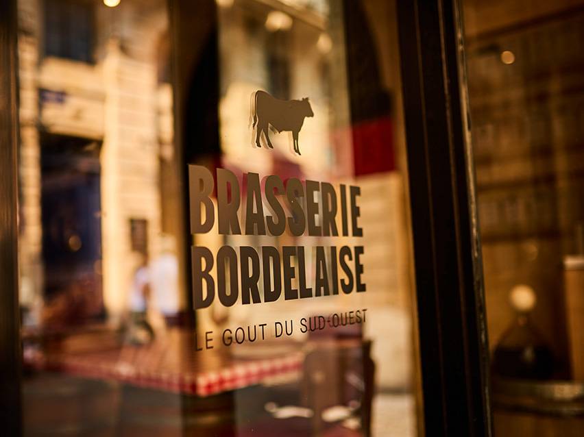 Insegna della Brasserie Bordelaise con sagoma di mucca e la scritta 'Le Goût du Sud-Ouest'.