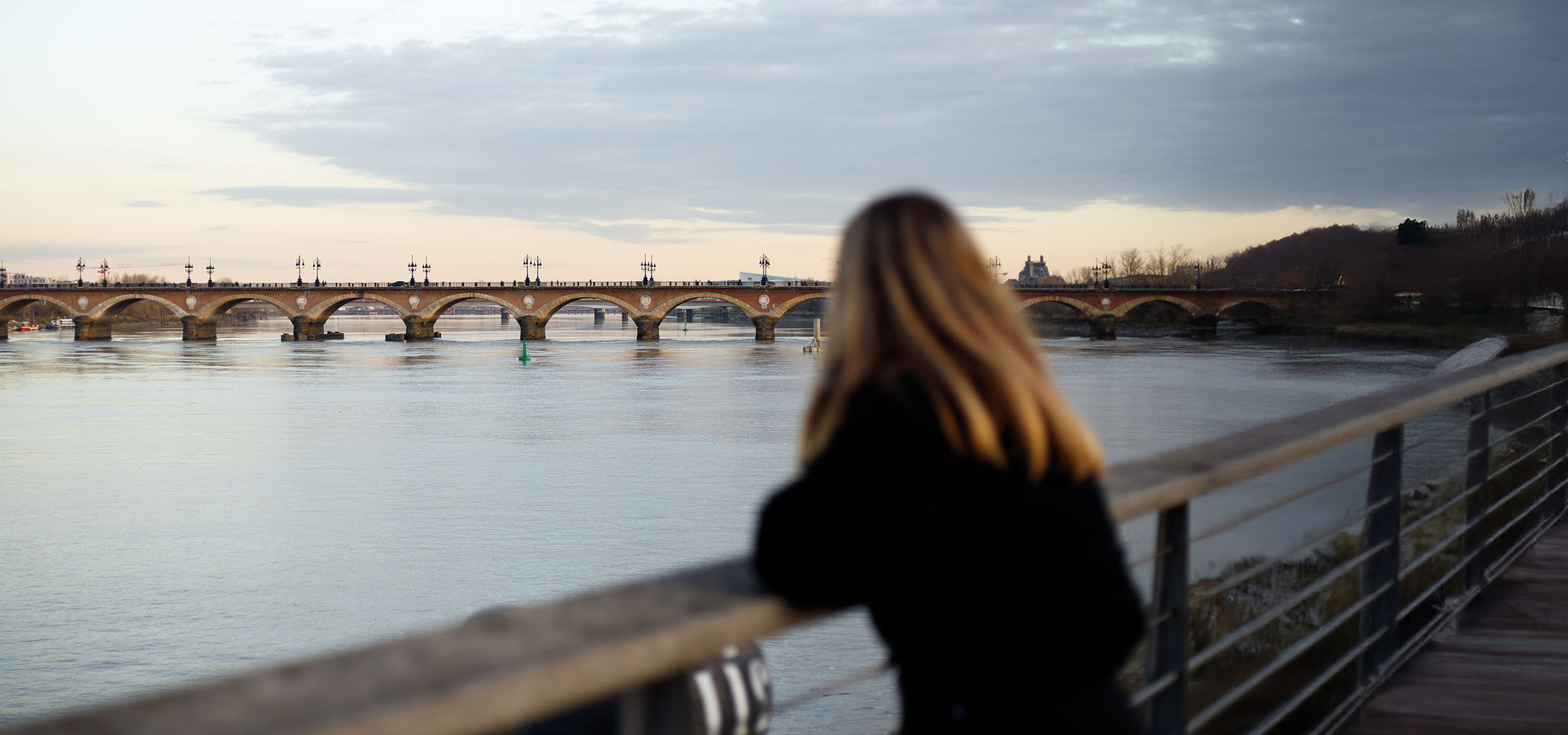 Vista di un ponte ad archi e un fiume, con una persona di spalle e capelli lunghi.