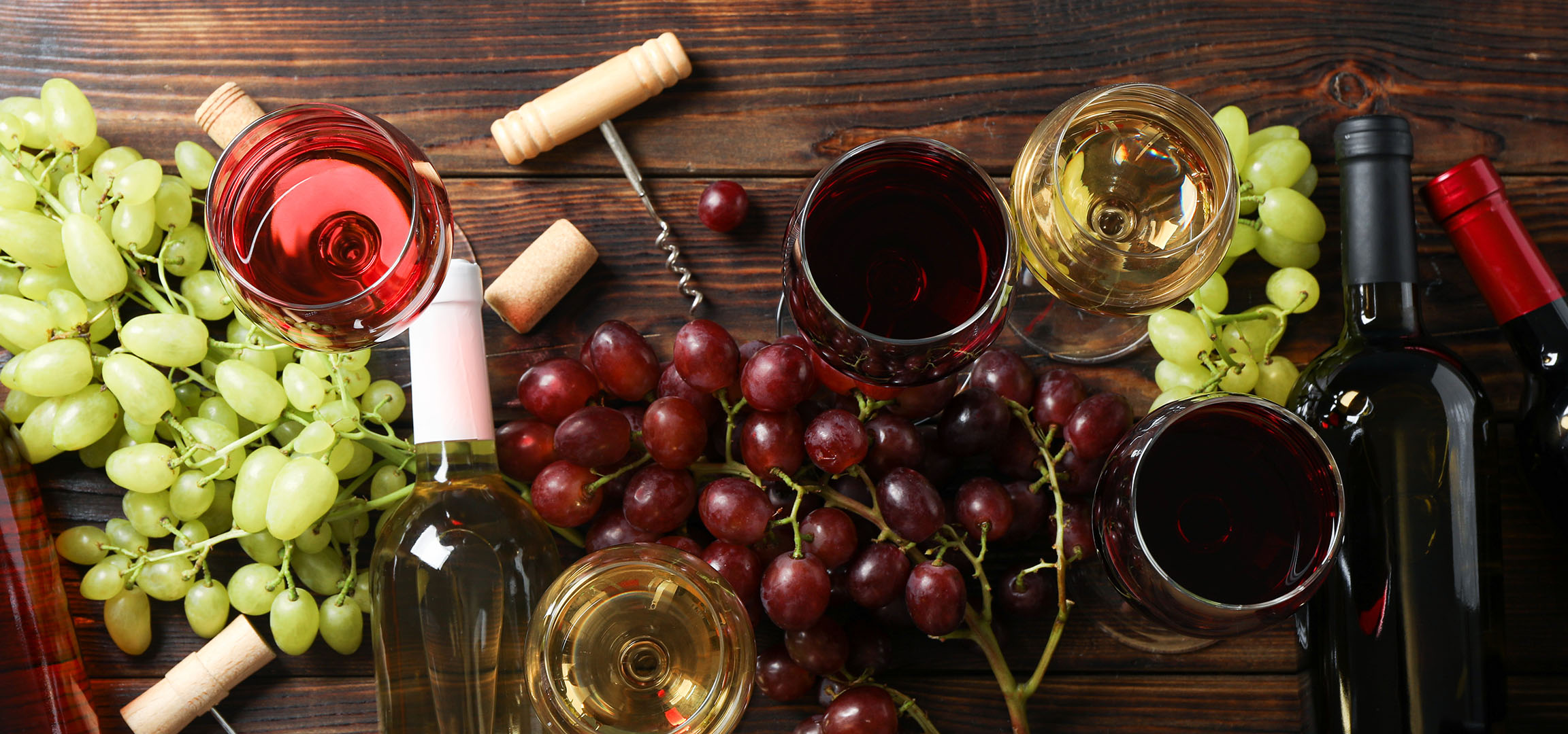 Vini assortiti, uva e accessori per il vino su un tavolo di legno.