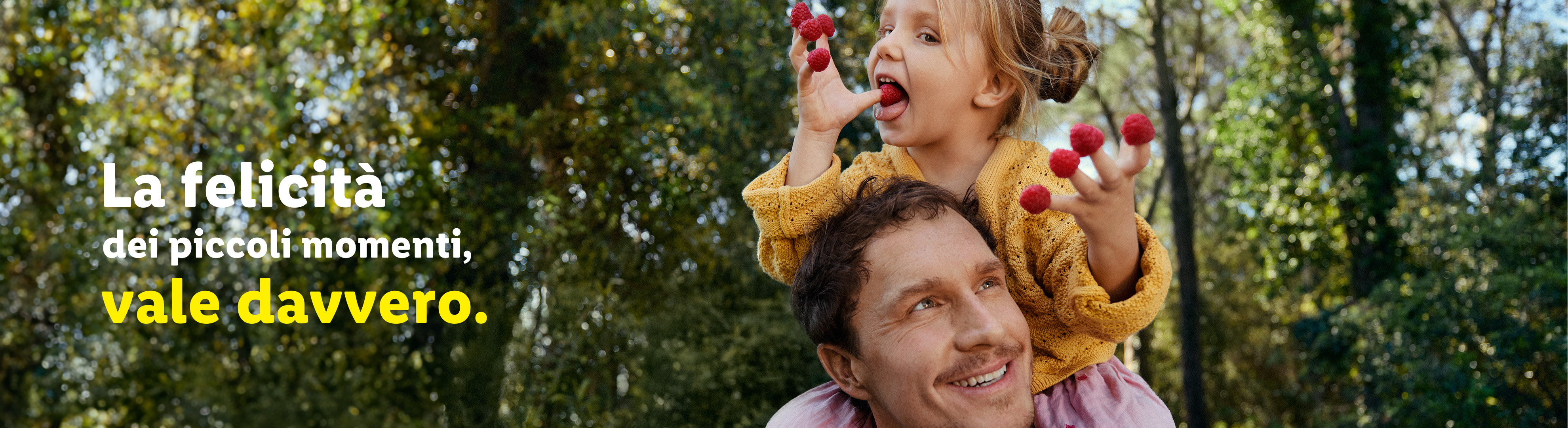 Un padre sorridente porta la figlia sulle spalle, che mangia lamponi.
