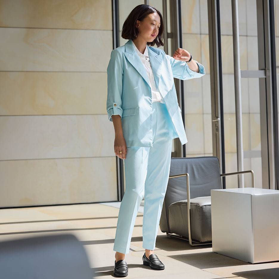 Donna in tailleur azzurro con blazer e pantaloni, indossa mocassini neri.