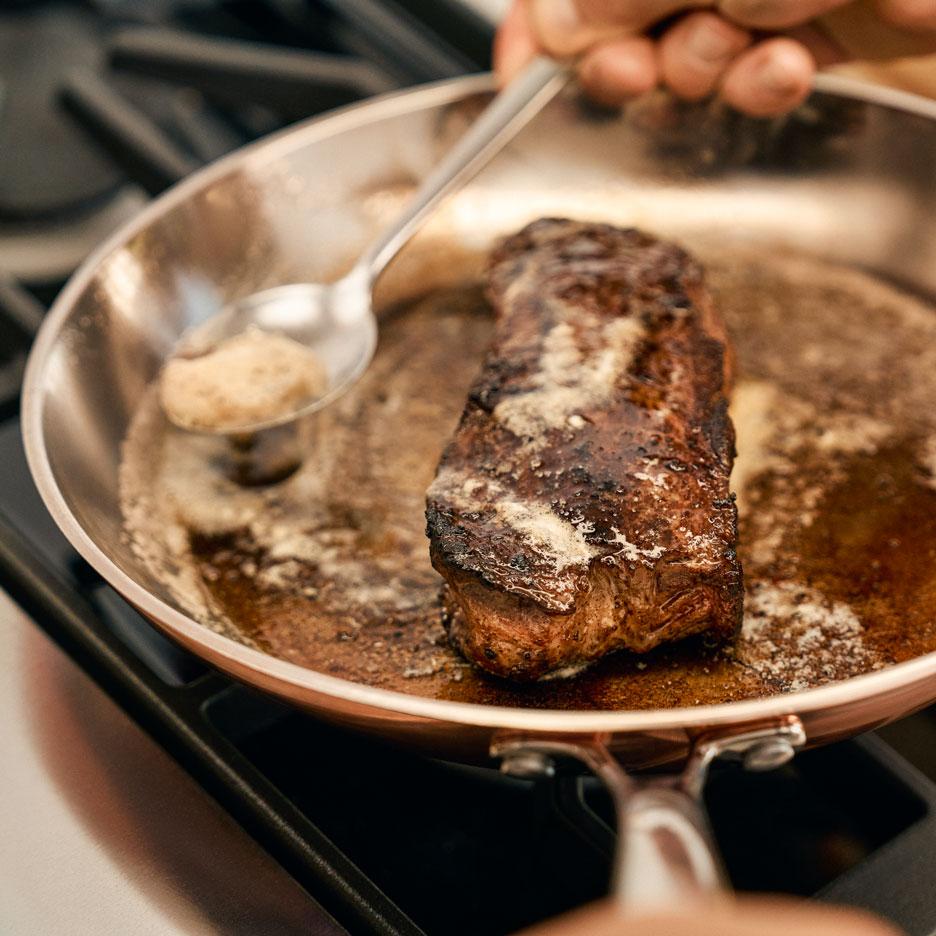 Una bistecca cuoce in padella con burro che viene versato sopra.