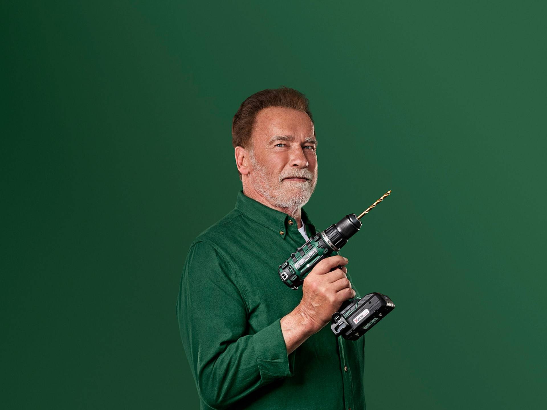 Arnold Schwarzenegger tiene un trapano elettrico verde su uno sfondo verde.
