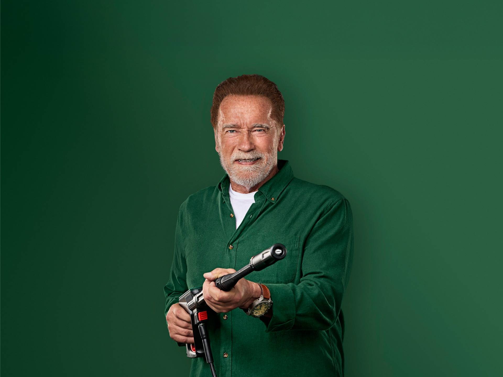 Arnold Schwarzenegger sorride, tenendo una pistola idropulitrice.