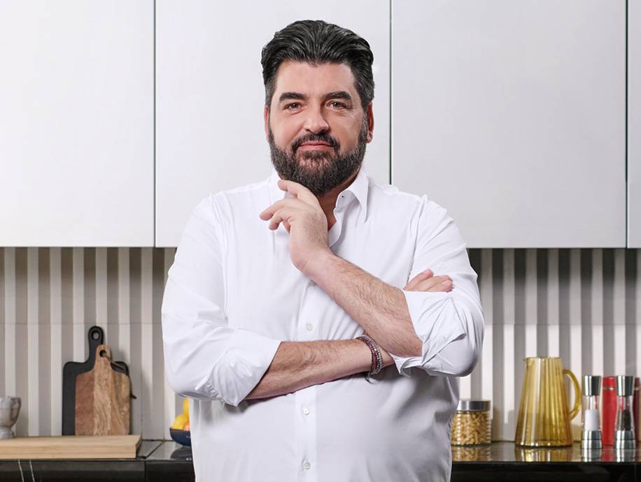 Uomo in camicia bianca in cucina con tagliere, brocca e spezie.