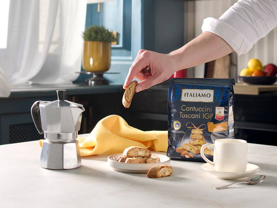 Moka, biscotti cantuccini e tazza di caffè su un tavolo, con una mano che prende un biscotto.