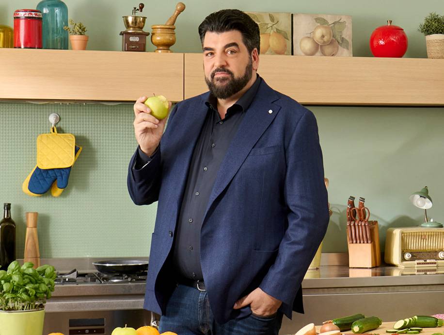 Uomo in cucina con mela verde, fornelli e utensili da cucina.