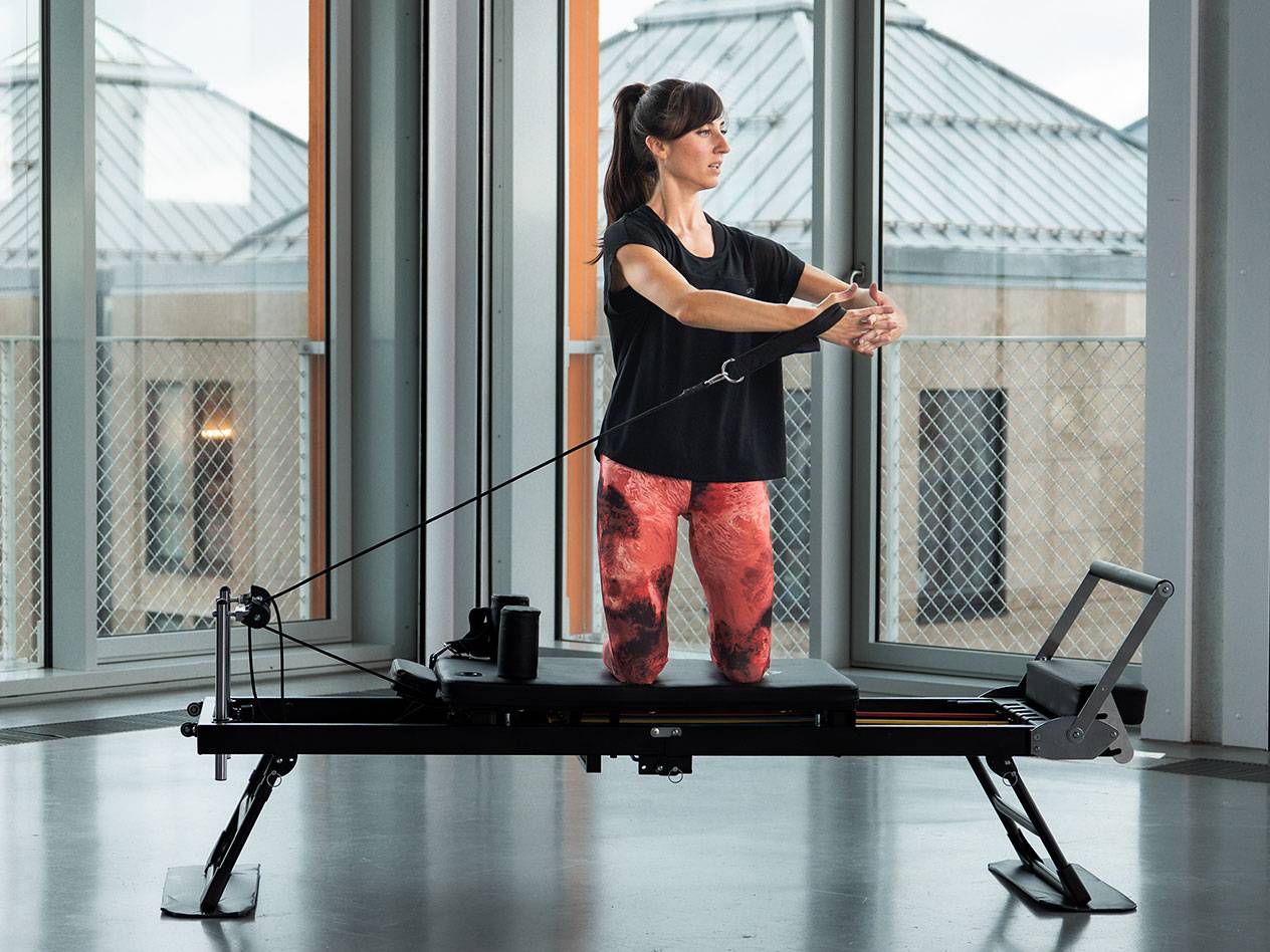 Donna che fa Pilates su una macchina reformer nera in una stanza luminosa.