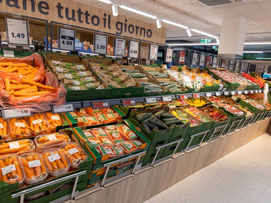 Un'ampia esposizione di frutta e verdura fresca, con carote in primo piano e cartelli dei prezzi.