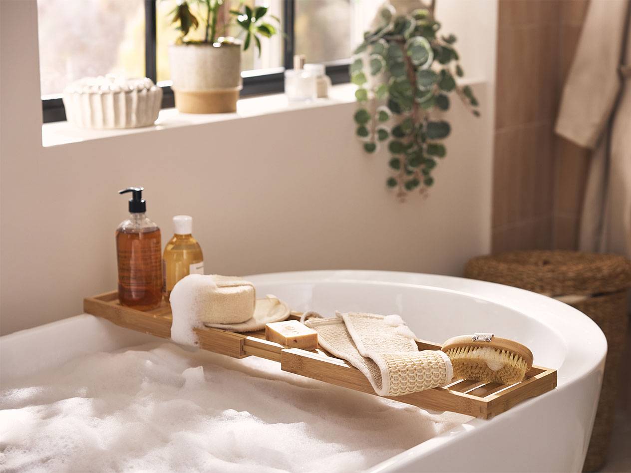 Vassoio da bagno in bambù con prodotti da bagno, spugne e spazzole sopra un bagno di schiuma.