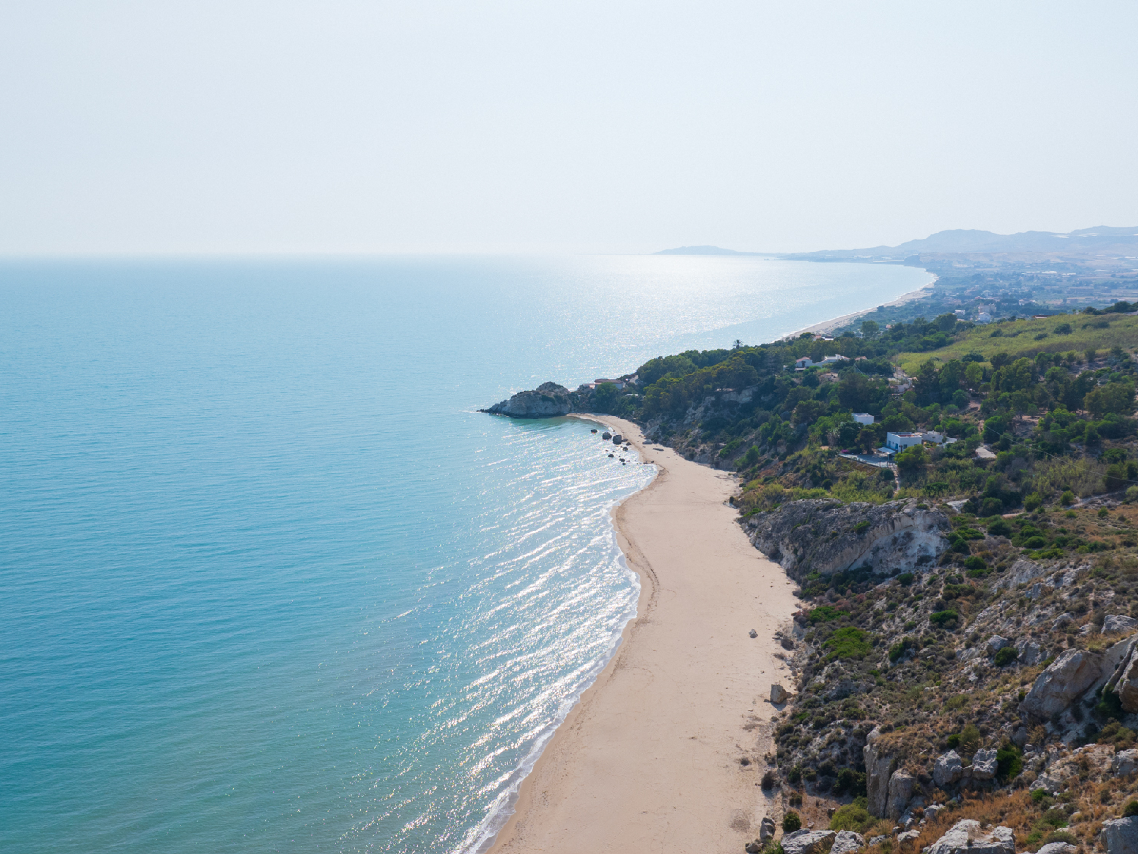 Spiaggia sabbiosa incontaminata con acque cristalline e vegetazione lussureggiante.