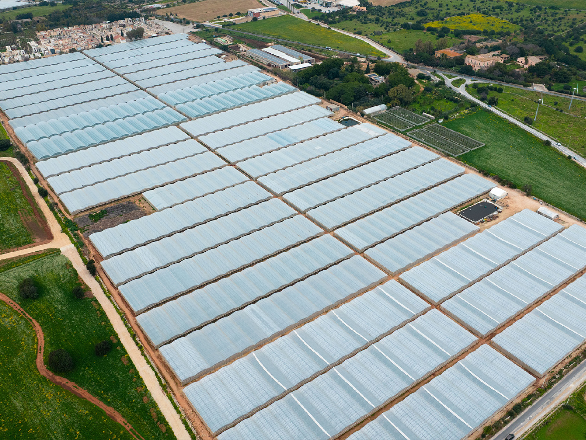 Serre agricole estese con campi verdi e strade, vista aerea.