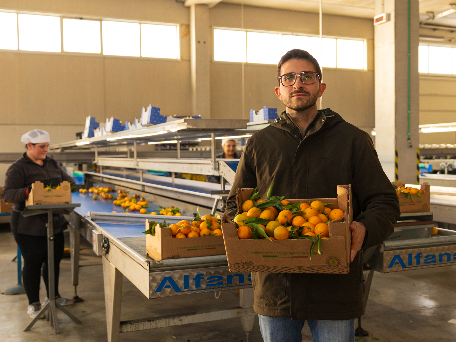 Uomo con occhiali tiene una cassetta di mandarini freschi in un magazzino di frutta.