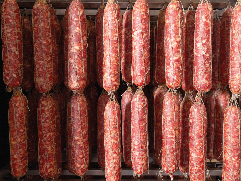 File di salami stagionati appesi ad asciugare in un salumificio.