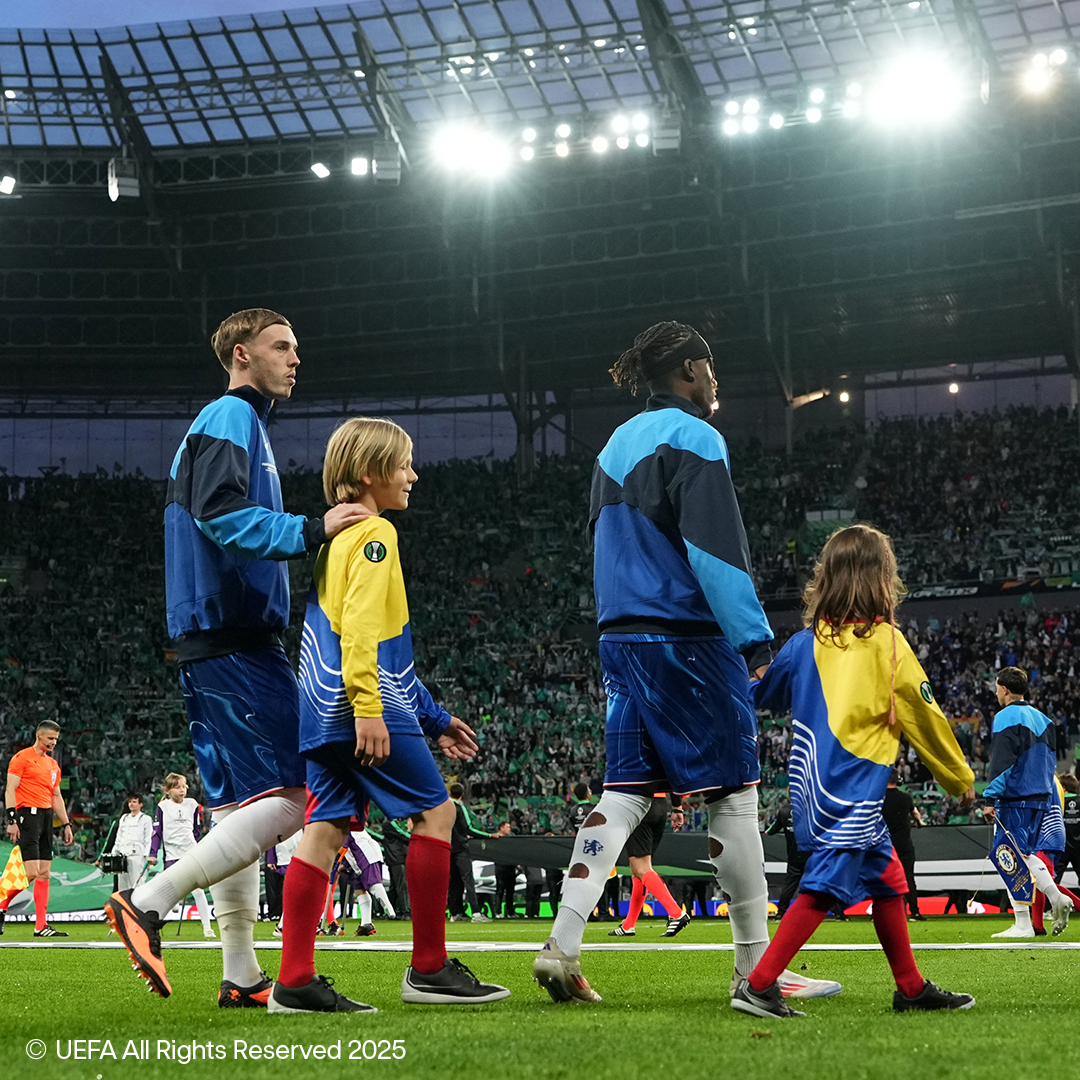 Calciatori e bambini camminano sul campo di uno stadio affollato.