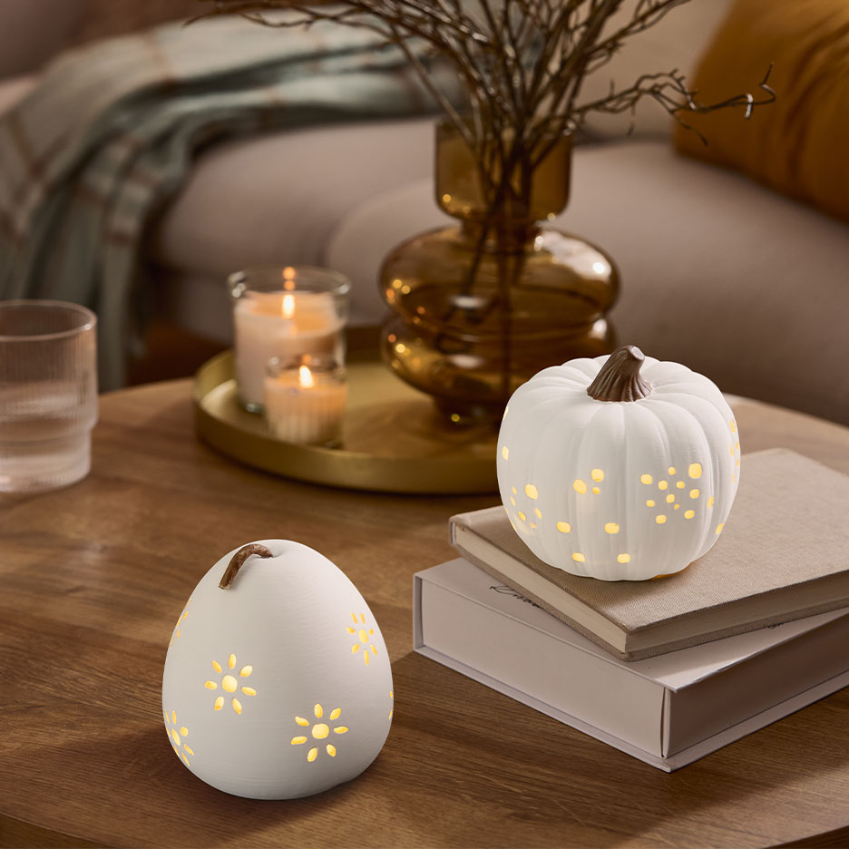 Due zucche decorative bianche illuminate su un tavolo di legno con candele e un vaso.