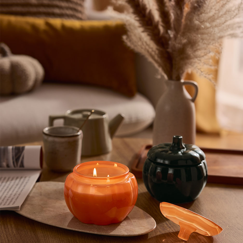 Candela e contenitore a forma di zucca su un tavolino da caffè con decorazioni autunnali.