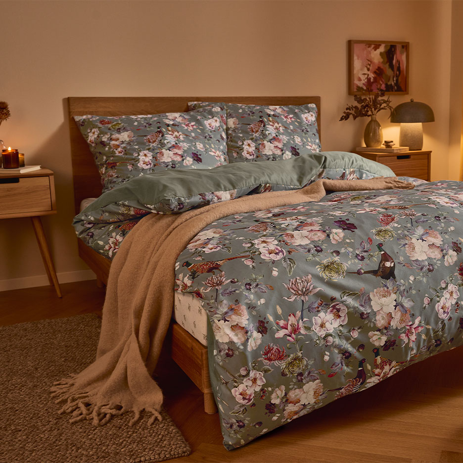 Letto in legno con biancheria da letto floreale verde e una coperta marrone.