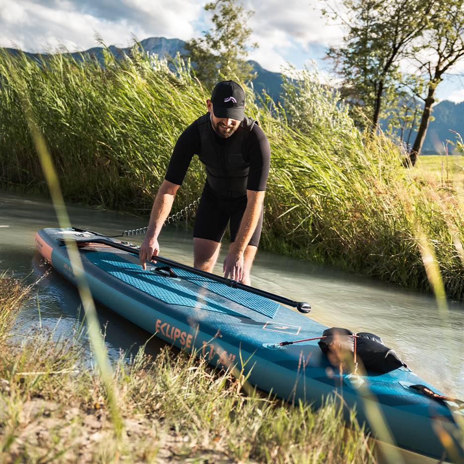 Uomo in muta nera si prepara per il paddleboard, tavola in acqua