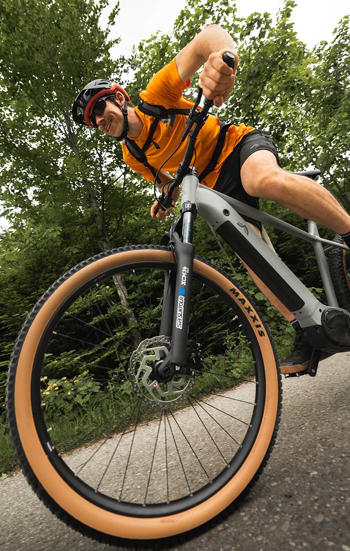 Un uomo va in bicicletta elettrica Maxxis grigia in un bosco.
