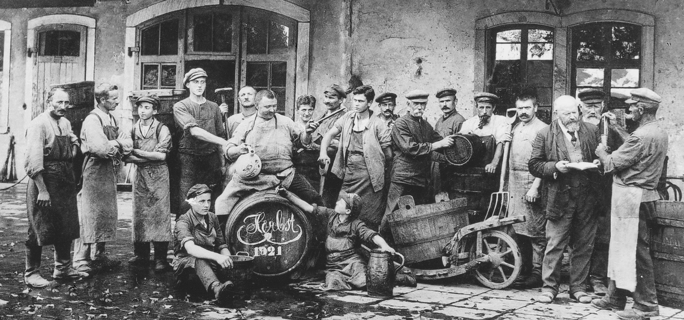 Uomini in una cantina con botti di vino, uno alza un bicchiere.