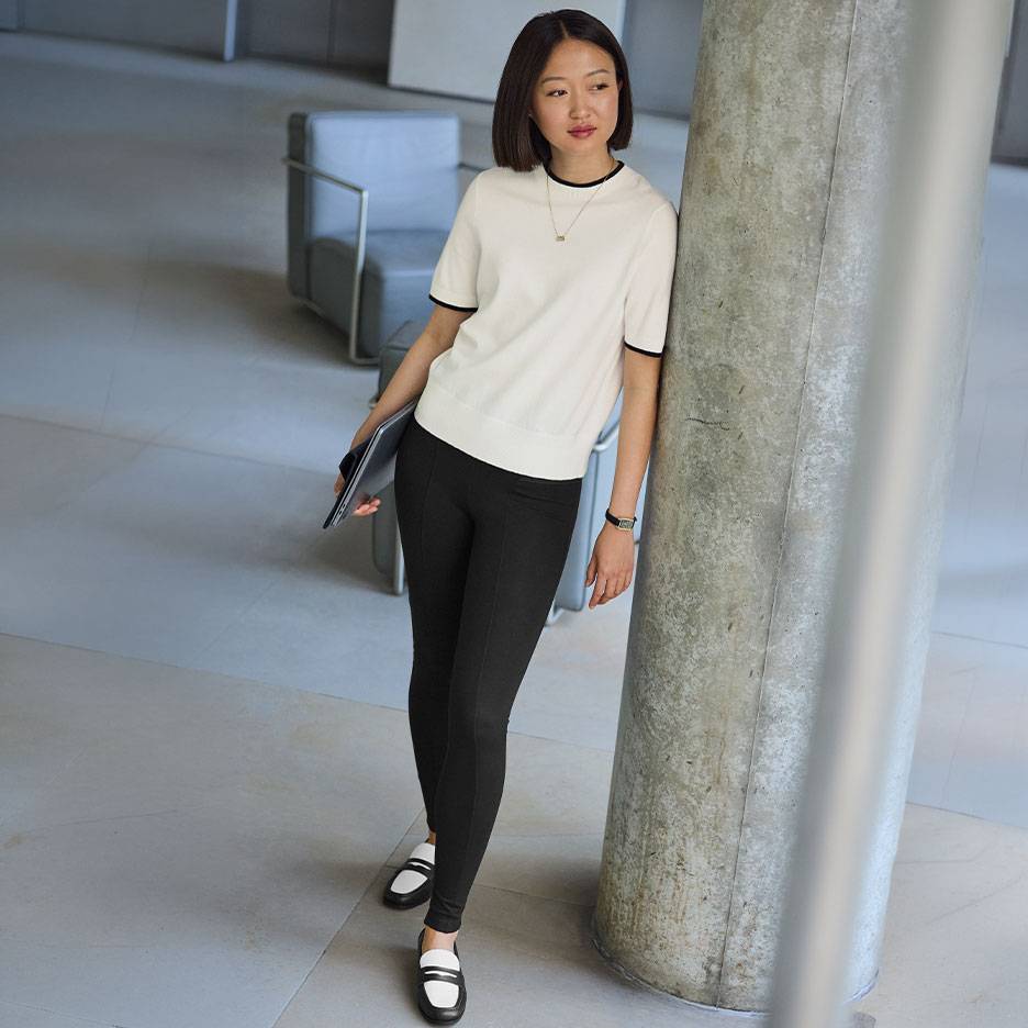Donna con top bianco a maniche corte con bordo nero, leggings neri e mocassini bicolore.