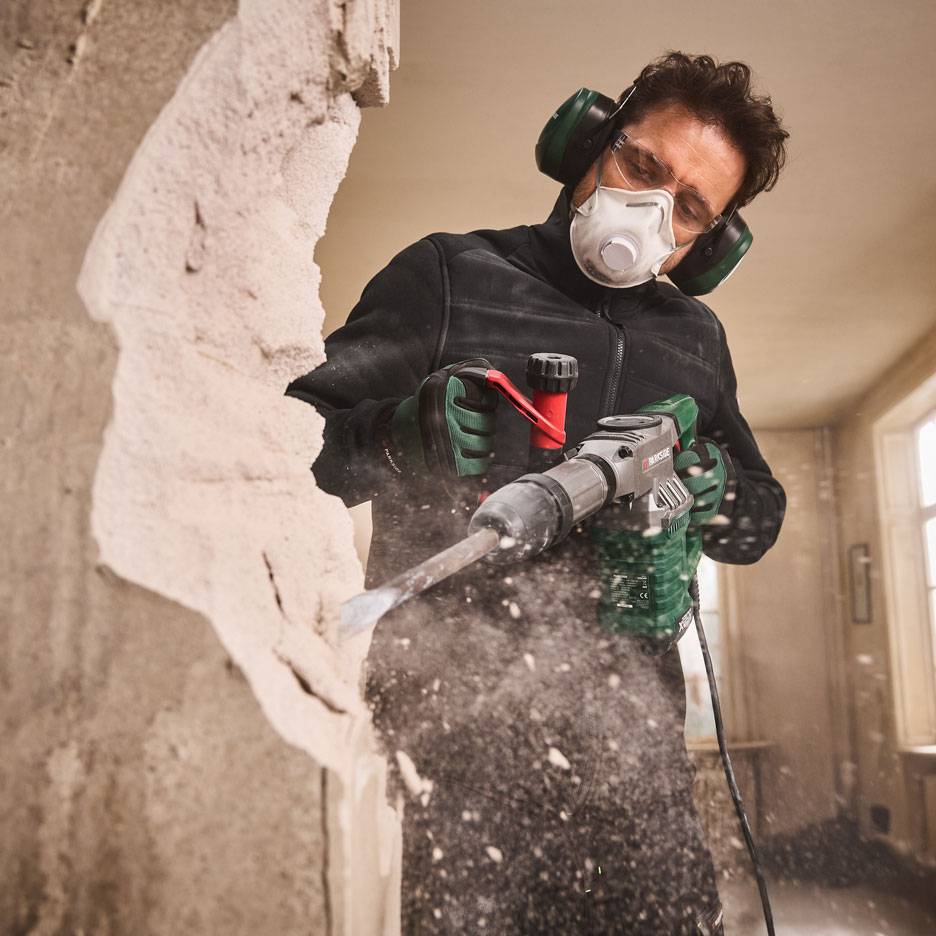 Uomo con martello demolitore e dispositivi di protezione mentre demolisce un muro.